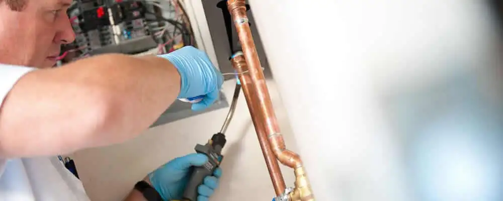 Water heater repair technician testing copper pipe connections and controls in Fort Wayne, IN